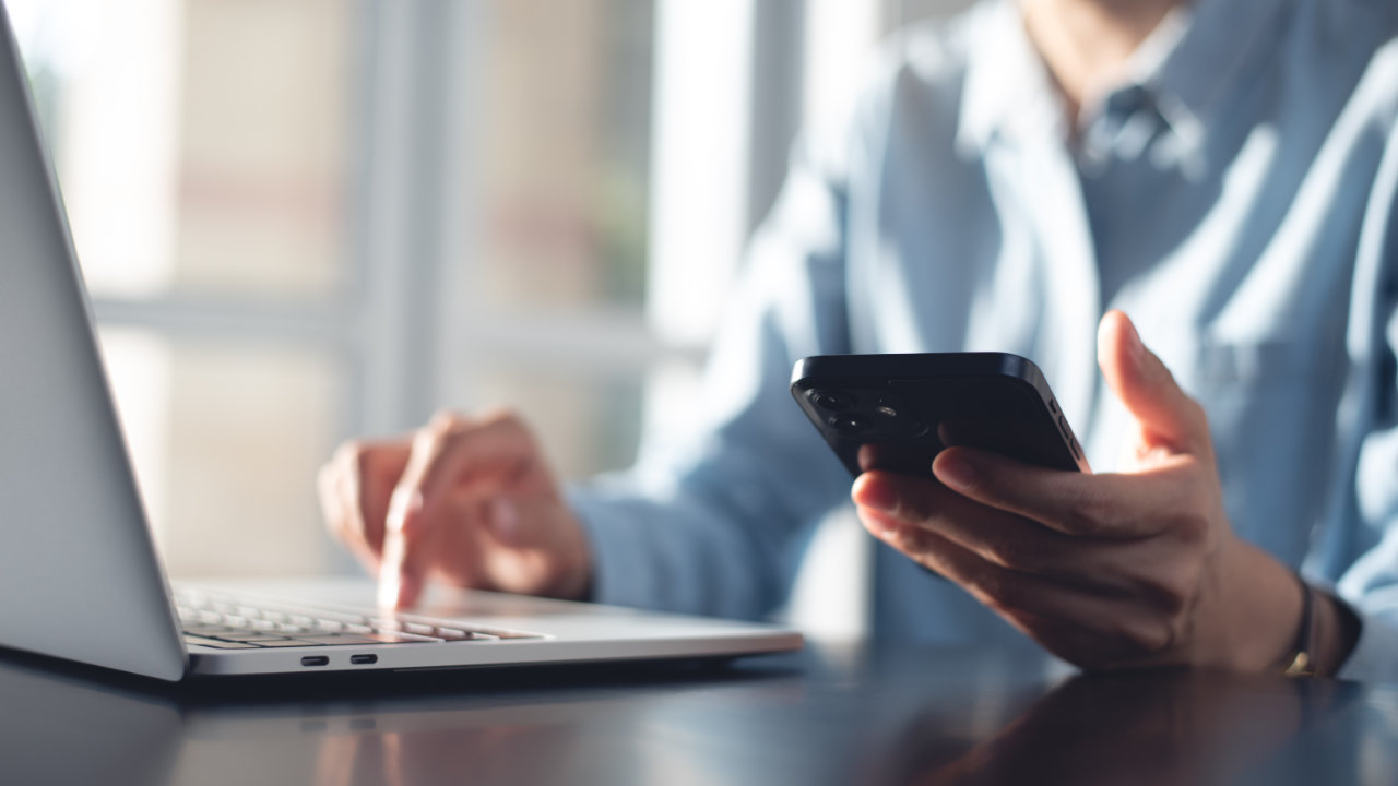 Person using a computer and holding a phone